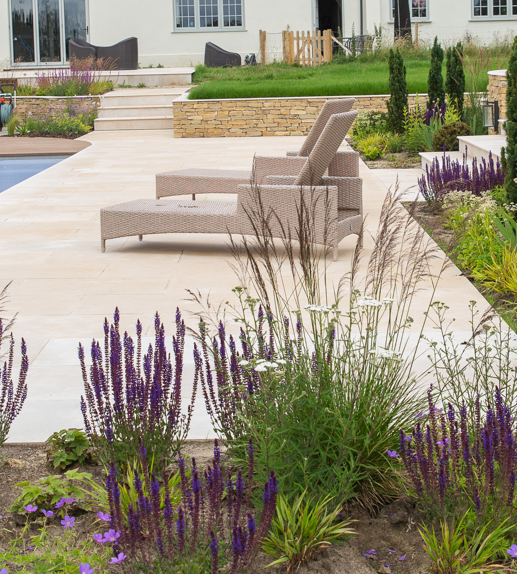A refined terrace softened by planted borders, with garden loungers beside a pool