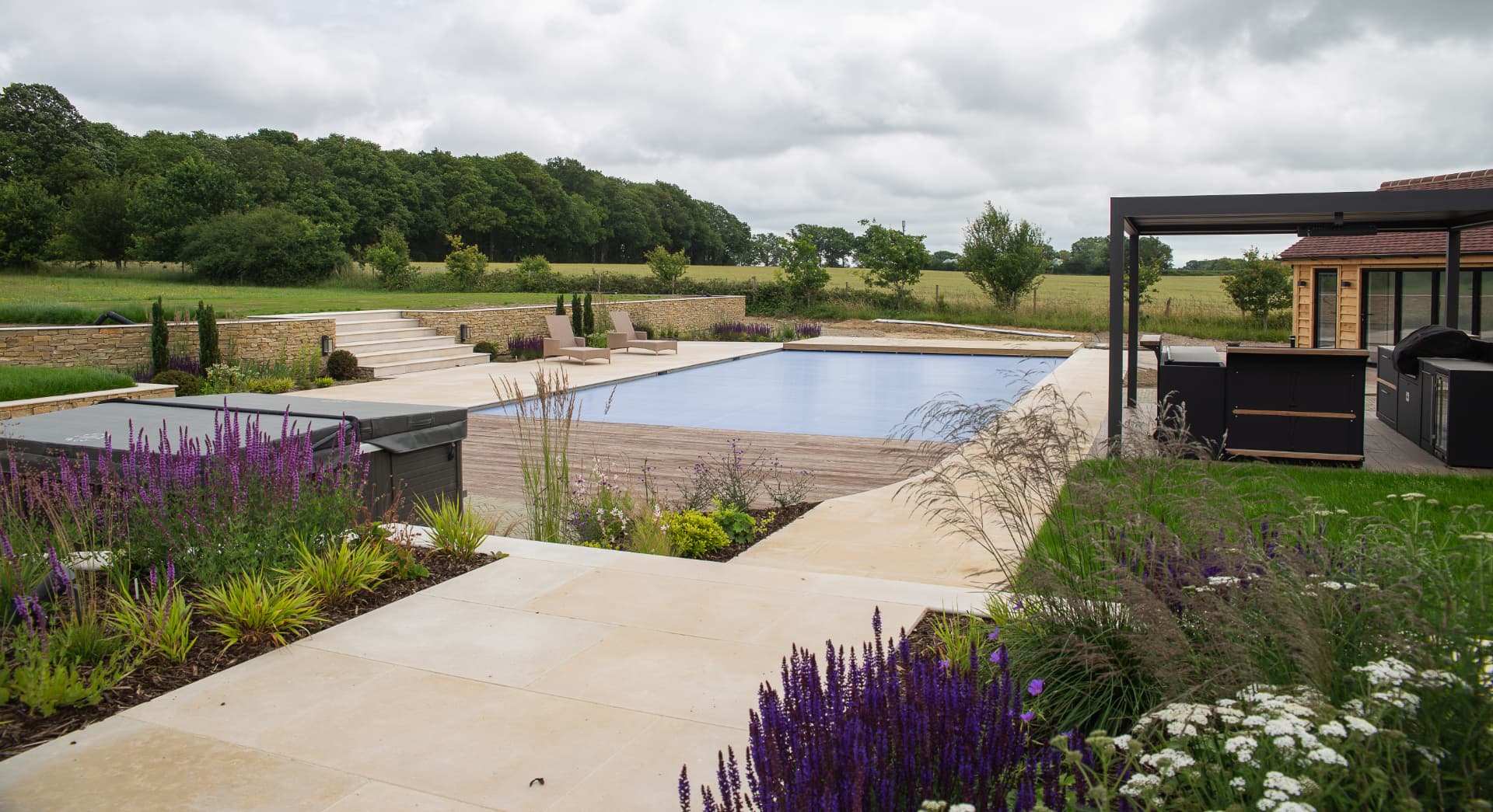 A poolside terrace finished with planted borders and soft landscaping against dry stone walling