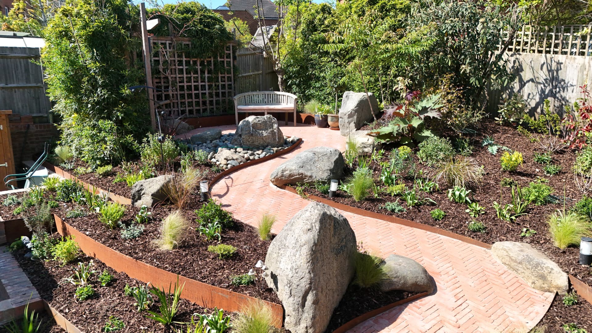 A gravel garden with boulders, mulched beds of grasses and perennials around a winding brick path