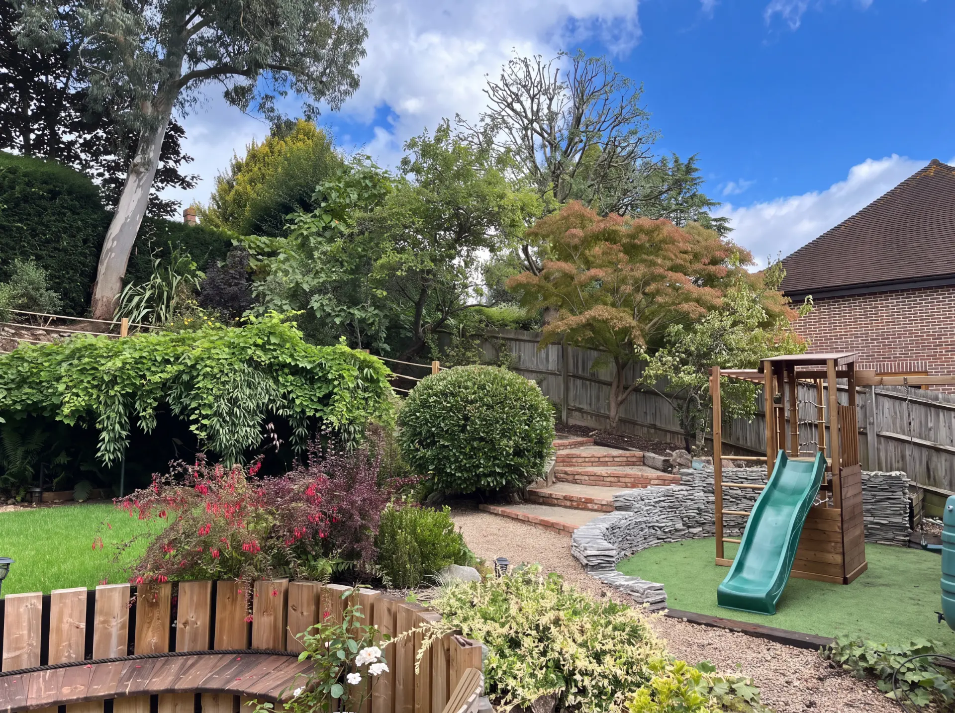 A family garden with a new lawn, planted borders and a play area beside dry stone walls