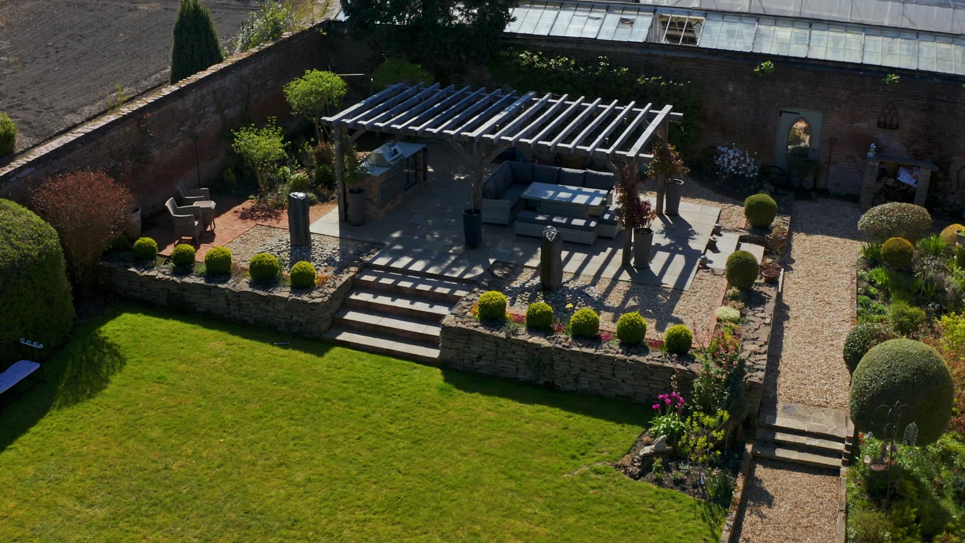 An elevated garden terrace with a pergola, seating and manicured lawns and planting
